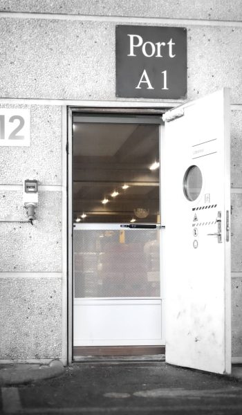 Lukket dør med insektnet og gitter monteret ved personaleindgang til lagerhal set udefra.