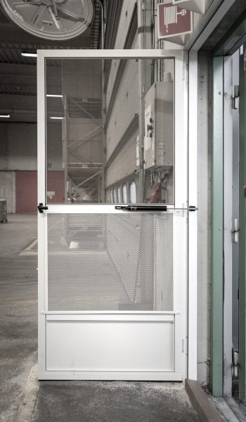 Åben dør med insektnet og gitter monteret ved personaleindgang til lagerhal set indefra.