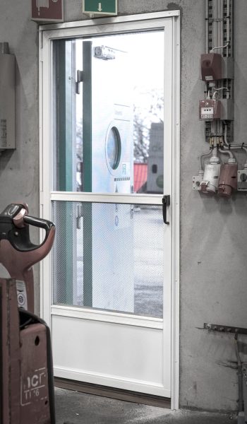 Lukket dør med insektnet og gitter monteret ved personaleindgang til lagerhal set indefra.